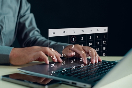 Hands typing on laptop with transparent digital calendar.