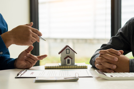 Two people talking with miniature home on a table.