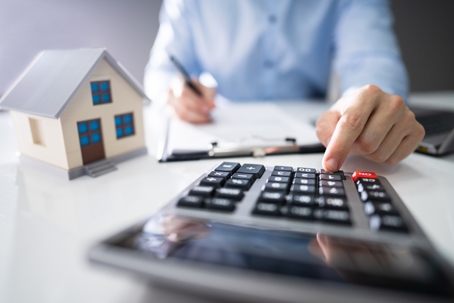 Person reviewing finances with a calculator and house model, representing bankruptcy planning and asset protection.