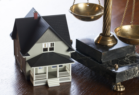 Model house beside a scale representing financial and legal housing decisions.